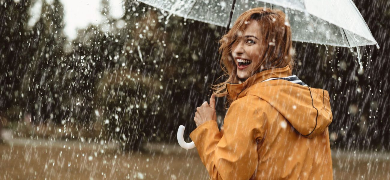 Cheerful pretty girl holding umbrella while strolling outside. She is turning back and looking at camera with true delight and sincere smile. Copy space in right side